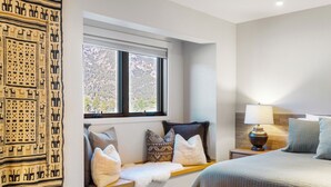 Un dormitorio con una cama grande, un asiento junto a la ventana con almohadones, una lámpara y un tapiz en la pared.