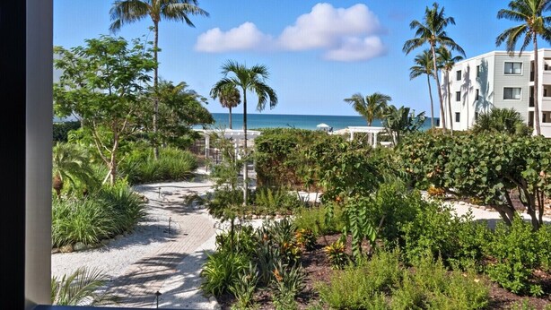 Un camino que lleva a una playa con palmeras y un edificio al fondo.