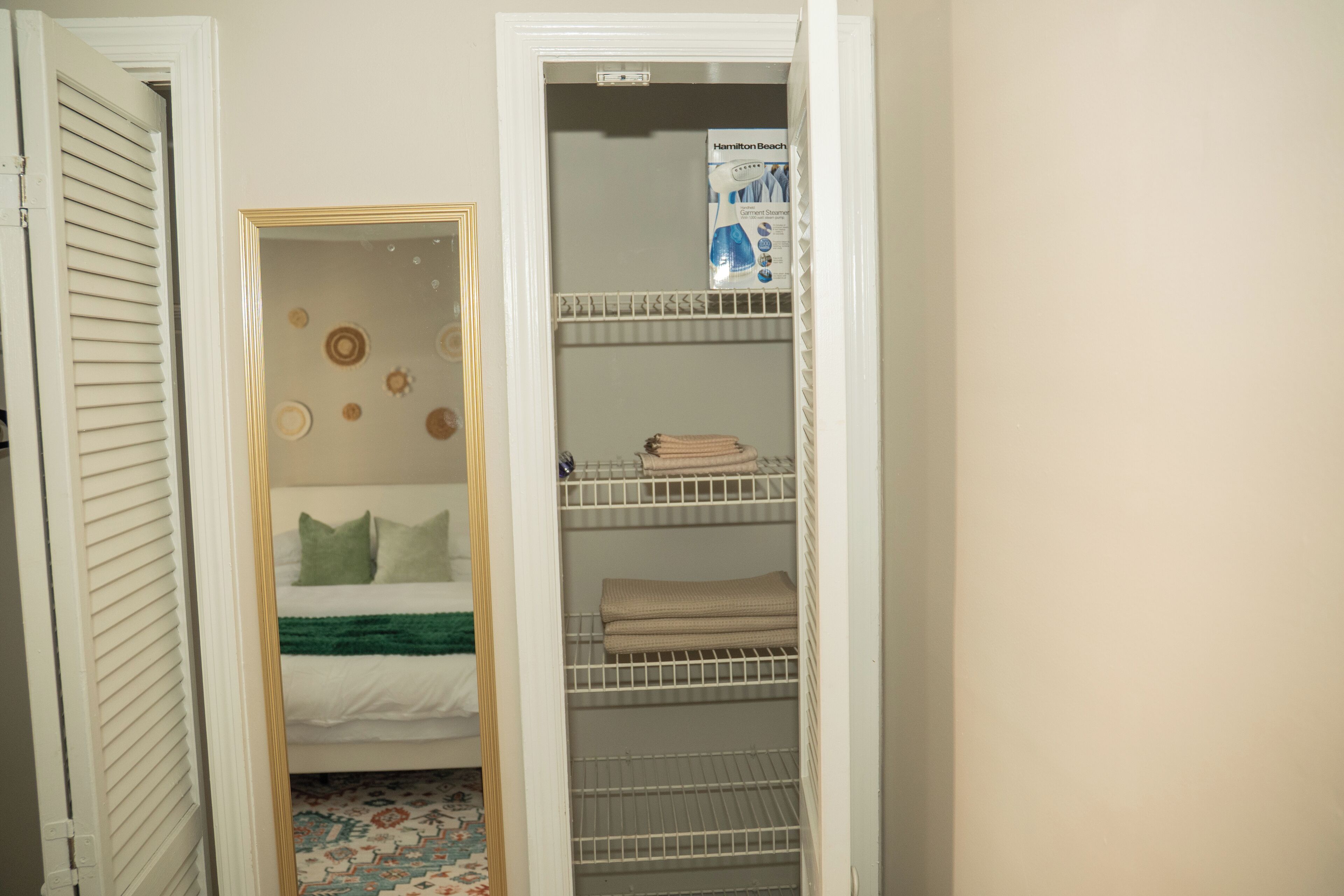 Armadio a muro con anta specchiata, mensole con asciugamani piegati e un letto con coperta verde.