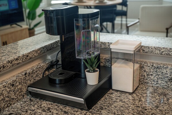 A kitchen with a coffee maker, a potted plant, and a container on the counter.