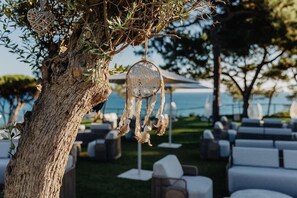 An outdoor seating area with white chairs and tables, a tree with hanging decorations, and a view of the sea. - W Residences Algarve (Albufeira)