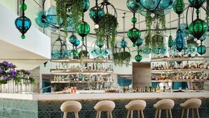 A bar area with hanging green glass chandeliers, bar stools, and shelves stocked with bottles.