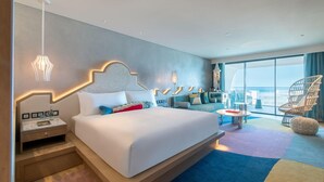 A modern hotel room with a large bed, a nightstand, a small table, a chair, and a view of the outdoors.