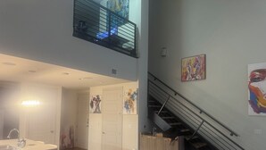 A spacious living area with a white sofa, a dining table with a modern light fixture, a staircase, and artwork on the walls. - Luxury Loft Penthouse in the Heart of the City with Skyline Views – 1BR, 1.5BA (Austin)