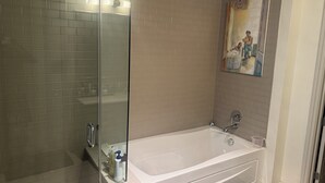A modern bathroom with a glass-enclosed shower, a white bathtub, and a painting on the wall. - Luxury Loft Penthouse in the Heart of the City with Skyline Views – 1BR, 1.5BA (Austin)