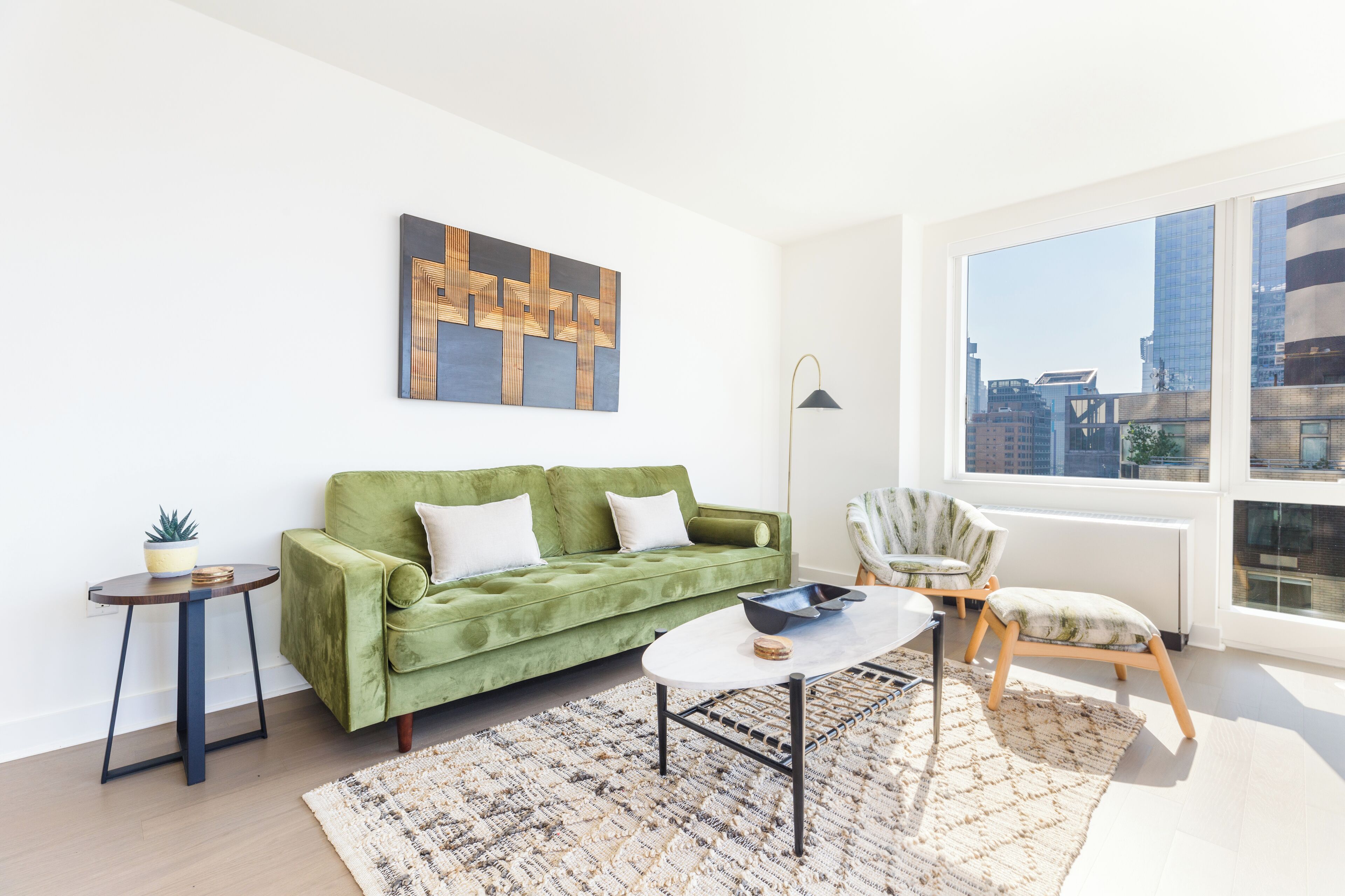 Un salón moderno con un sofá verde, una mesa redonda de centro y vistas a la ciudad a través de amplias ventanas.