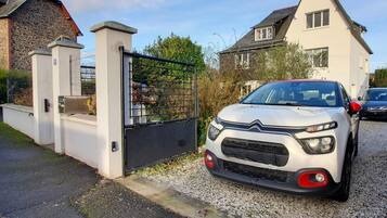 A white car parked in a driveway with a gated entrance, a house in the background, and a gravel path.