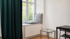 A corner room with a window, radiator, small table, and chair. - Karolkowa City Comfort Studio (Warszawa)