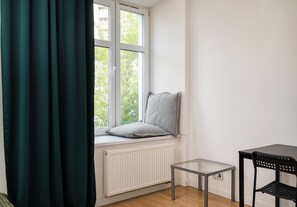 A corner room with a window, radiator, small table, and chair.