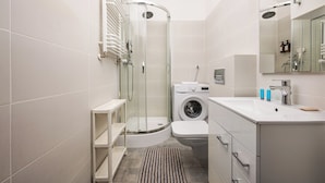 A modern bathroom with a glass-enclosed shower, a washing machine, and a sink with a mirror. - Karolkowa City Comfort Studio (Warszawa)