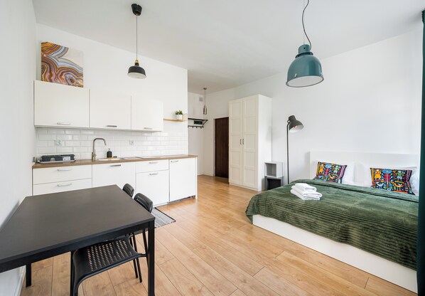 A modern room with a kitchen, dining area, and a bed with colorful pillows.
