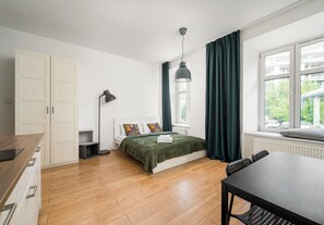 Een slaapkamer met een bed, een bureau, een stoel, een kledingkast, een radiator en een raam met gordijnen.