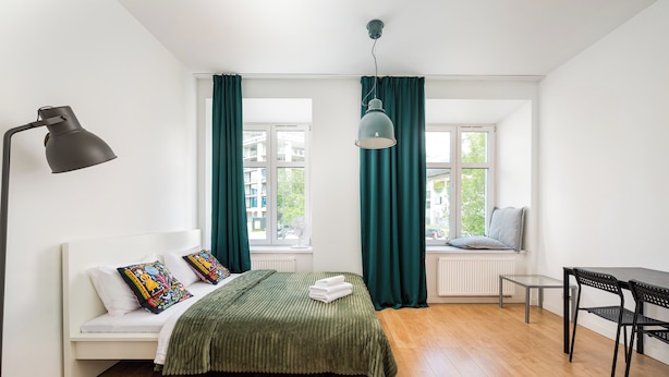 A room with a bed, a desk, a chair, a lamp, and a window with curtains. - Karolkowa City Comfort Studio (Warszawa)