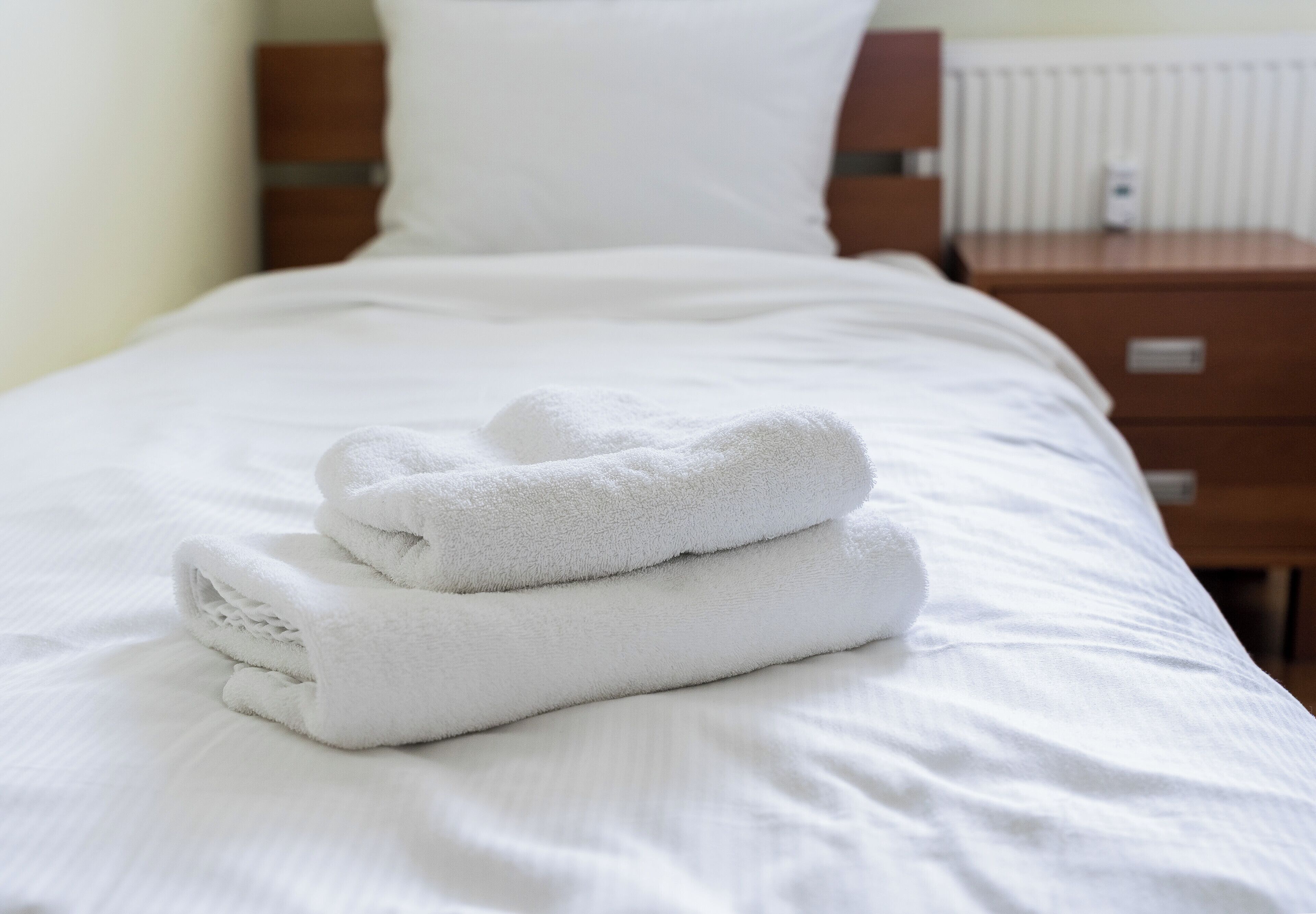 Ein ordentlich bezogenes Bett mit weißen Laken und einem gefalteten weißen Handtuch.