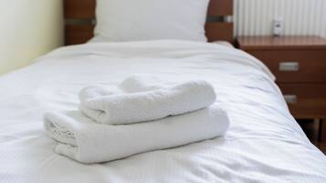 Ein ordentlich bezogenes Bett mit weißen Laken und einem gefalteten weißen Handtuch.
