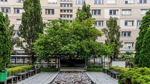 Een binnentuin met een centraal waterpartij, omringd door bankjes en begroeiing, met een meerhoog gebouw op de achtergrond.