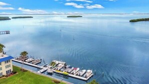 A marina with boats docked, a building with a blue roof, and calm water with islands in the distance. - Beautiful 2 BR Condo With Private Beach Access Sunset On The Gulf (Longboat Key)