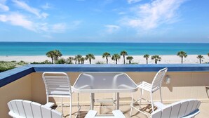 Un balcon avec une table et des chaises donnant sur une plage bordée de palmiers et sur l’océan.