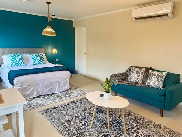 Un dormitorio moderno con una cama, un sofá azul verdoso, una mesita de centro blanca y una lámpara colgante.