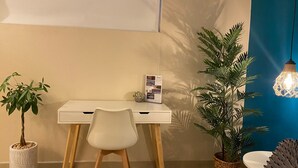 A bedroom with a bed, a desk with a chair, a potted plant, a wall-mounted light fixture, and a wall calendar.