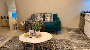 A living room with a sofa, a coffee table, a potted plant, a clock, and a stove.