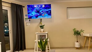 A room with a TV mounted on the wall, a small table with a plant, a remote control, and a sign with a prohibition symbol.