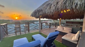 An outdoor deck with lounge chairs and a thatched roof structure, overlooking a body of water.