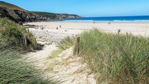 Une plage avec un ciel dégagé, des falaises rocheuses et un sentier sablonneux menant à la rive.