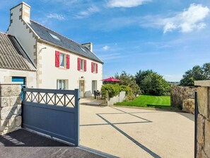A two-story house with a stone facade, red shutters, and a paved driveway leading to a gated entrance. - De cap en cap by Interhome (Cléden Cap Sizun)