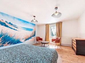 A bedroom with a large bed, two chairs, a small table, a dresser, and a beach mural on the wall. - De cap en cap by Interhome (Cléden Cap Sizun)