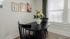 A dining area with a black table and chairs, a vase with flowers, and framed artwork on the wall.