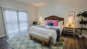 A bedroom with a bed, bedside tables, a bench, a window with curtains, and a potted plant.