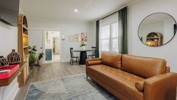 A living room with a brown leather sofa, a round mirror, and a dining area with a table and chairs.