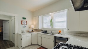 A kitchen with white cabinets, a gas stove, a sink, and a window with blinds.