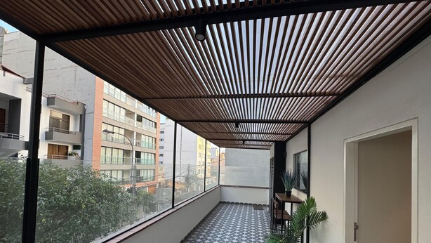 A balcony with a patterned floor, a wooden ceiling, and a view of surrounding buildings.