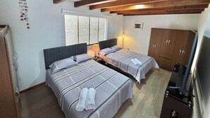 A room with two beds, wooden beams, a window, a wardrobe, and a television.