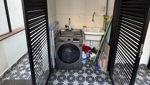 A compact laundry room with a washing machine, sink, and storage shelves.