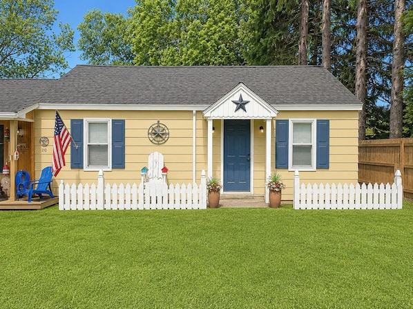 A single-story house with a blue door, a white picket fence, and a star on the front.