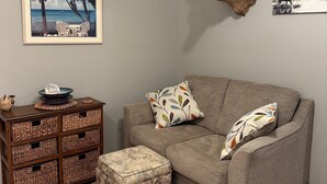 Ein Wohnzimmer mit grauem Sofa, gemusterten Kissen, einem dekorativen Hirschgeweih, einem gerahmten Foto vom Strand, einem Holztisch mit einer Schale und Korbspeicherkisten.