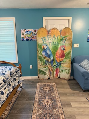 A bedroom with a bed, a blue sofa, a decorative wooden partition with parrots, a patterned rug, and a door.
