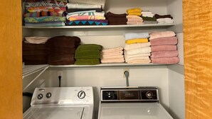 Un cuarto de lavandería con lavadora y secadora apiladas, repisas con toallas dobladas y un enchufe.