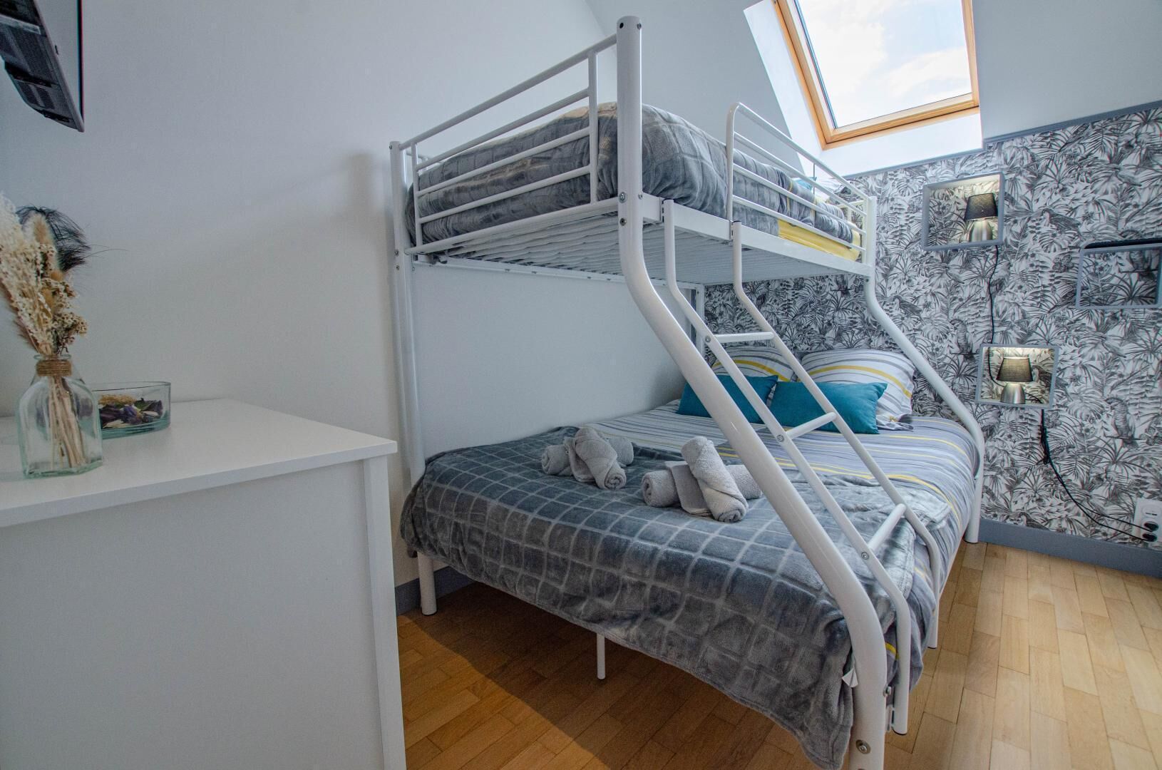 A bunk bed room with a skylight, a shelf with decorative items, and a patterned wall.