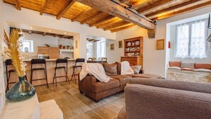 A cozy living room with a brown sofa, a kitchen area with a brick wall, and a stone fireplace. - Gite de la Tour - LES RICEYS (LES RICEYS)