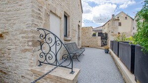 A narrow alleyway with stone buildings, a metal bench, and a gated area with plants. - Gite de la Tour - LES RICEYS (LES RICEYS)