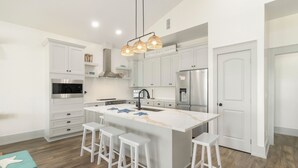 Cocina moderna con armarios blancos, una isla central con taburetes de bar, electrodomésticos de acero inoxidable y una lámpara colgante.
