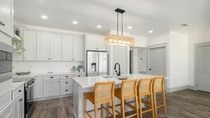 Een moderne keuken met witte kasten, een centraal eiland met barstoelen, een roestvrijstalen koelkast en een hangende lamp.