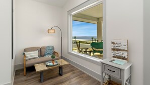 Ett modernt rum med ett stort fönster, en soffa, ett litet bord, en lampa och en skylt som är upphängd på väggen.