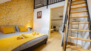 A bedroom with a bed, a wooden ladder, a nightstand, and a wall with floral wallpaper. - Gite Seigneurial - LES RICEYS (LES RICEYS)