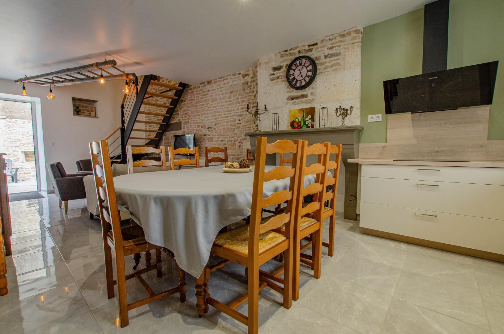 Ein Essbereich mit Backsteinwand, Holzkästen, einem Tisch mit Tischdecke, einer Uhr und einer Küchenzeile mit Herd.