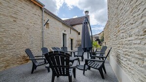 An outdoor patio with a table and chairs, a covered umbrella, and a stone wall. - Gite Seigneurial - LES RICEYS (LES RICEYS)